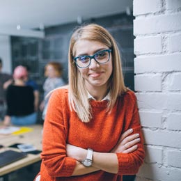 junge Frau mit Brille und verschränkten Armen an Wand gelehnt