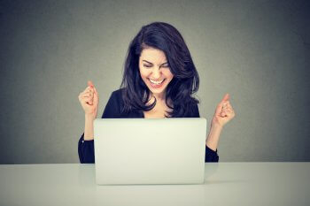 junge Frau sitzt vor dem Laptop und freut sich